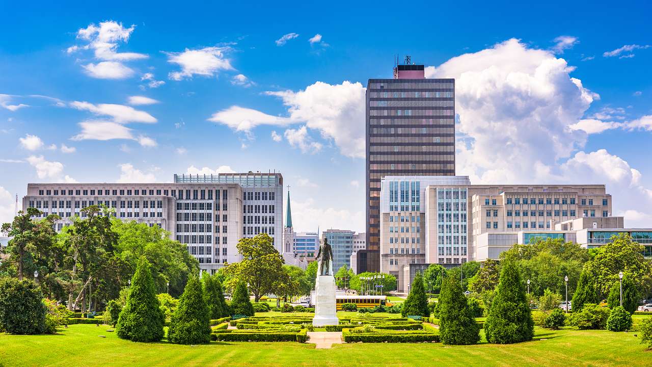 Skyline of tall modern buildings overlooking a statue of a man surrounded by trees