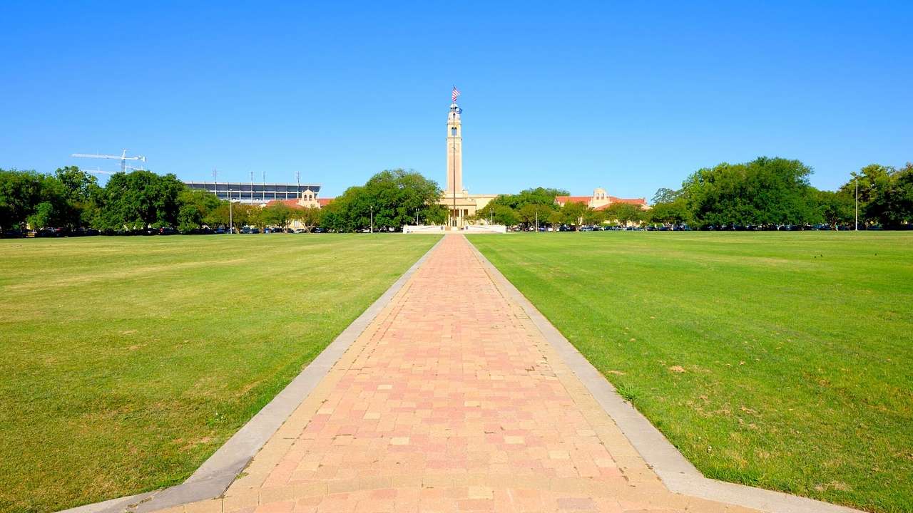 A walkway between green grass, leading to a concrete tower building under a blue sky