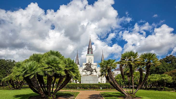 A path with grass and trees on either side and a statue and cathedral behind it