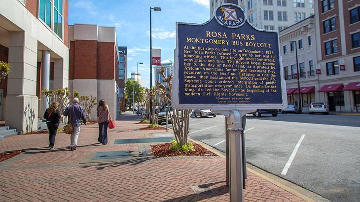 A metal sign on a sidewalk in a city with buildings in the background