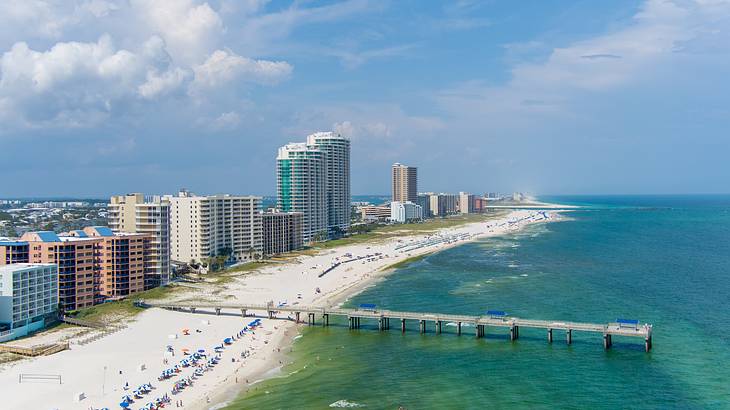 A boardwalk extending from a sandy white beach of a coastal city with tall buildings