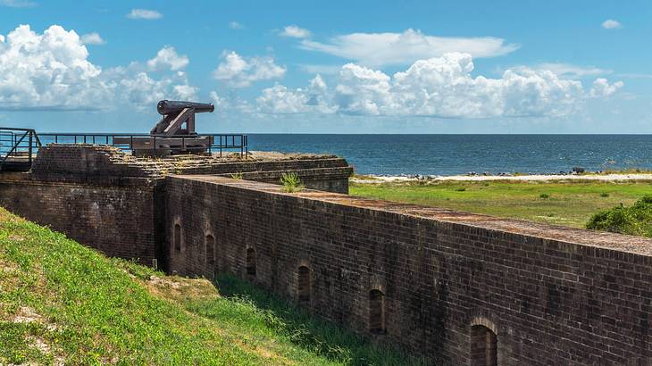 A black cannon on the brick wall of a fort overlooking the sea