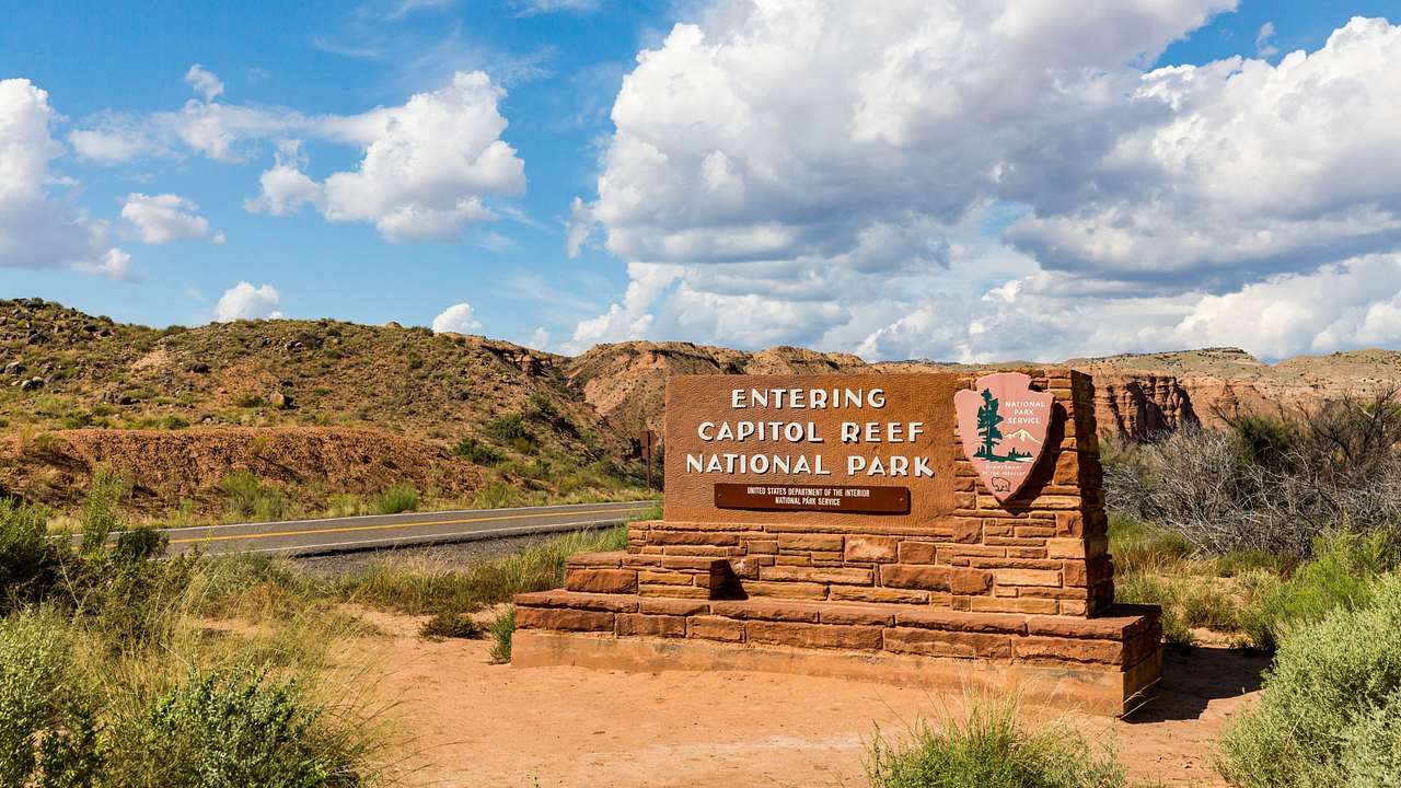 A sign that says "Entering Capital Reef National Park" next to greenery-covered hills