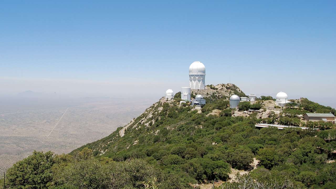 White and gray domes atop a tree-covered mountain overlooking a valley