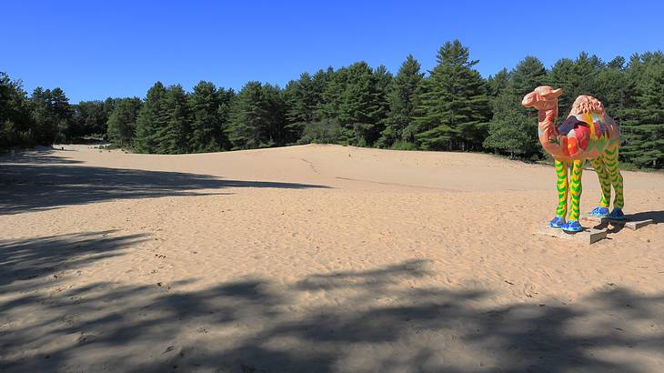 A sandy area with trees and blue sky at the back, and a camel statue on the right