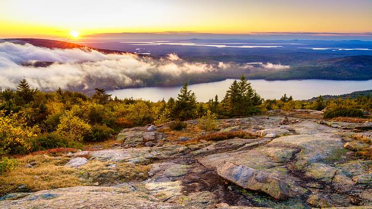 A landscape of rocks and trees with clouds, fog, and water in the distance