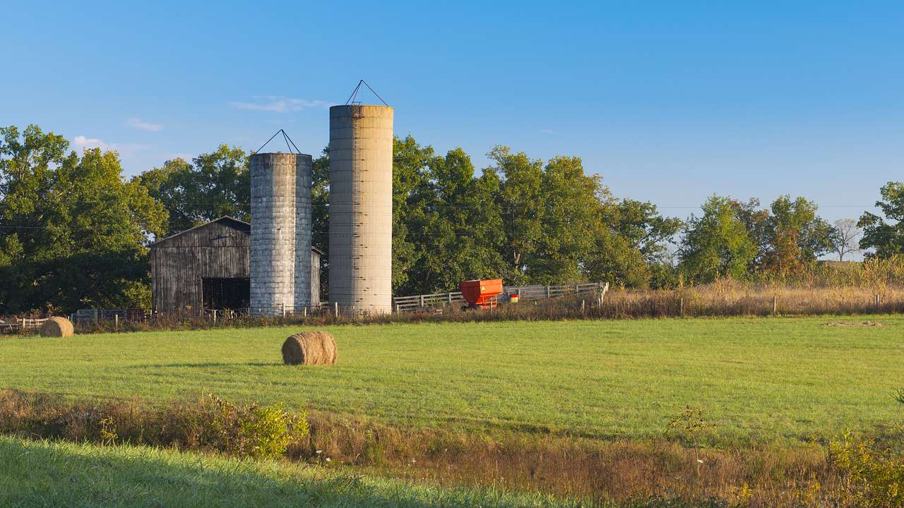 Silos, a wooden barn, and a red wagon on a farm surrounded by trees
