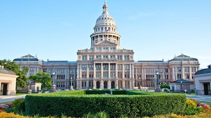 A large white building with green hedges in front on a nice day