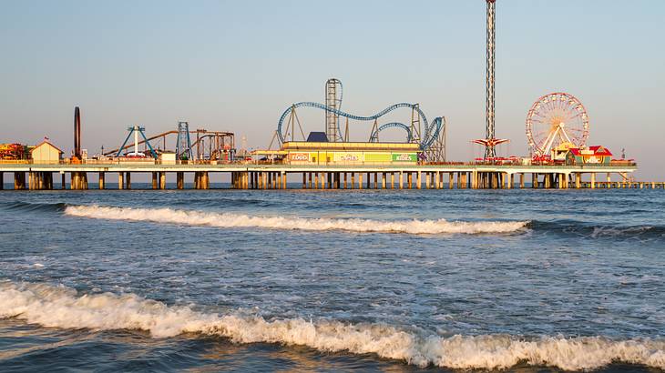 Roller coasters in a theme park next to a body of water on a clear day