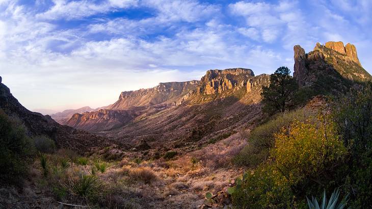 A rocky mountain range with dry green bushes in a valley and a blue sky