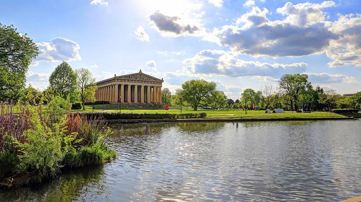 A columned building near a body of water, green grass and trees, and blue sky