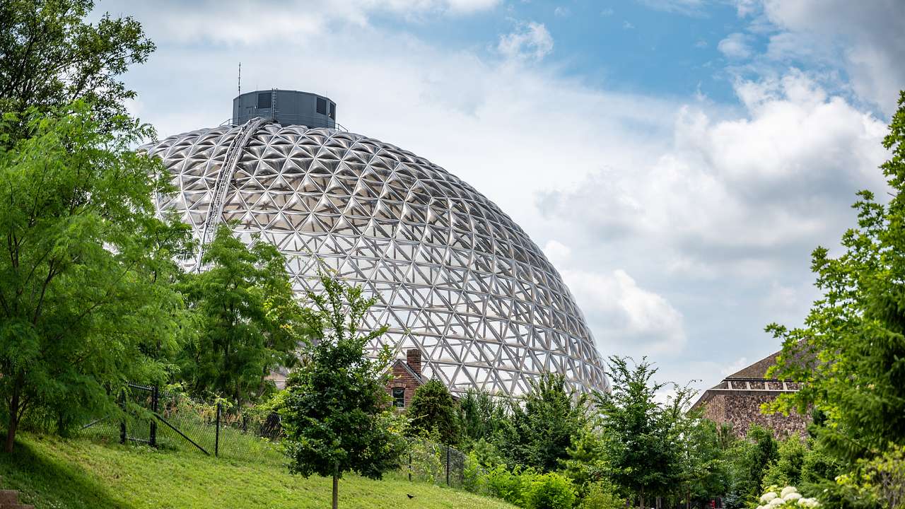 A dome made of steel and glass surrounded by trees and plants