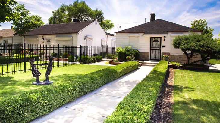 A pathway between green grass to a vernacular white house with a black roof
