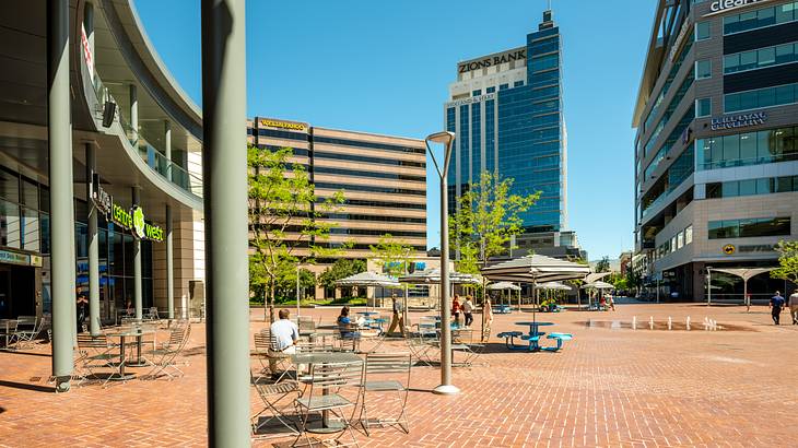 A pedestrian square with chairs under patio umbrellas against tall glass buildings