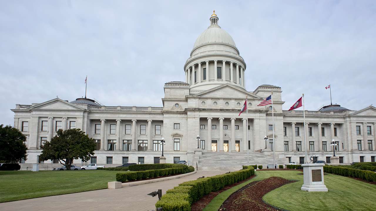 A white capitol building with a dome and a garden in front, under a cloudy sky