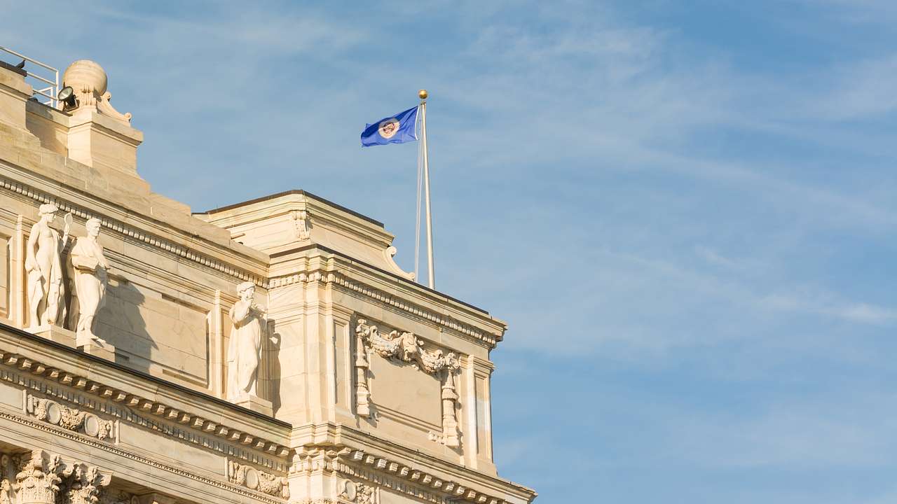A flag atop a historic white building against a blue sky with light white clouds
