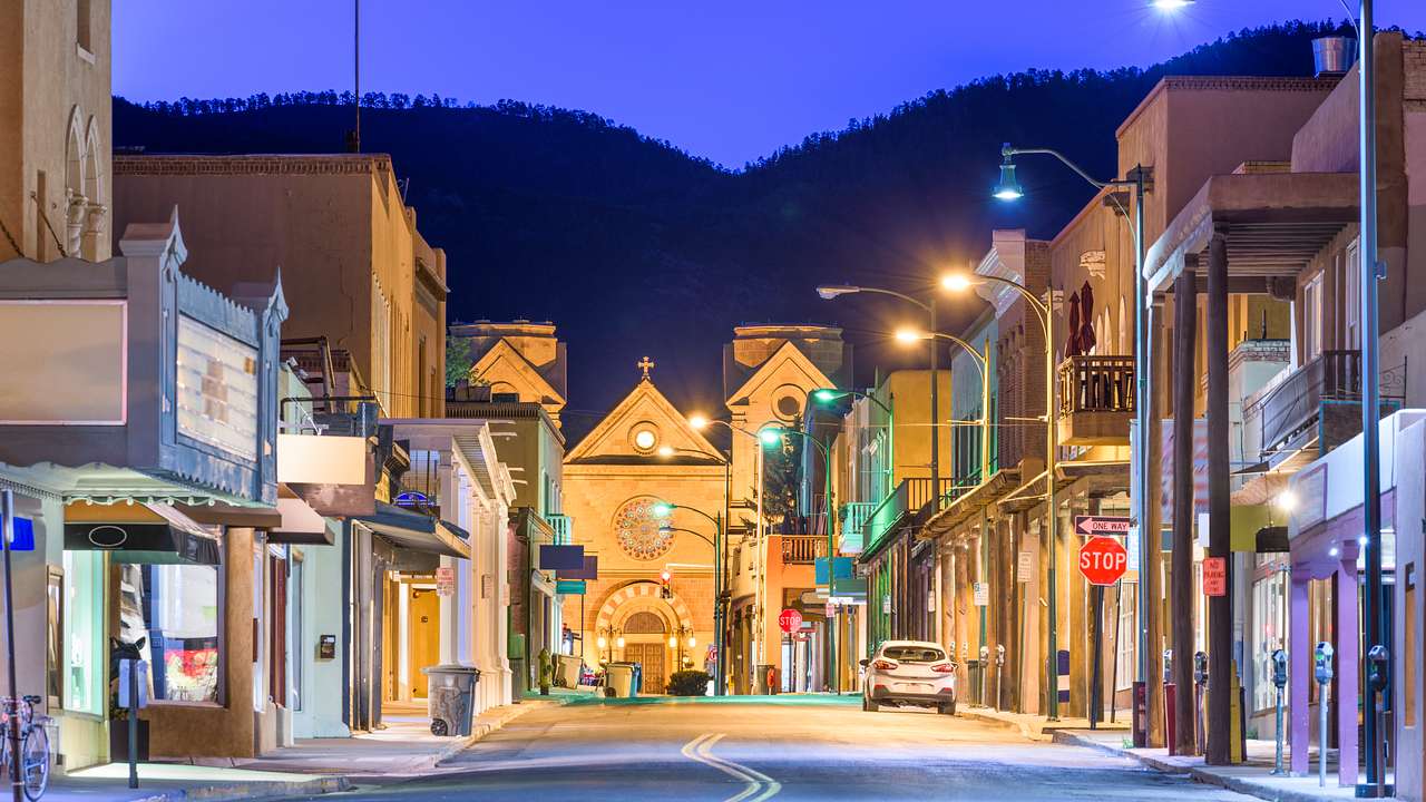 A street with a car and lit-up shops on each side against a mountain at night
