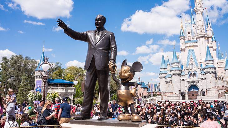 A statue of Walt Disney holding Mickey Mouse's hand while waving at people