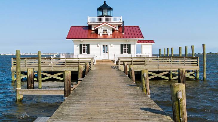 A red and white lighthouse at the end of a dock over water A red and white lighthouse at the end of a dock over water