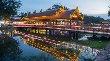 een verlicht gebouw en een brug over water met mensen die er in de schemering op lopen