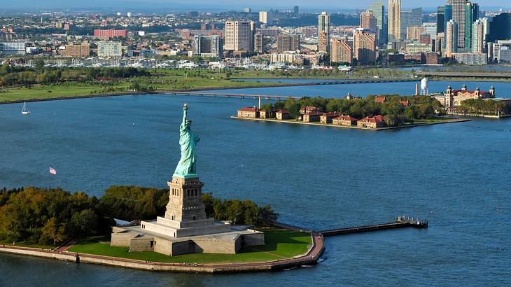 The Statue of Liberty with water surrounding it and a city skyline in the distance