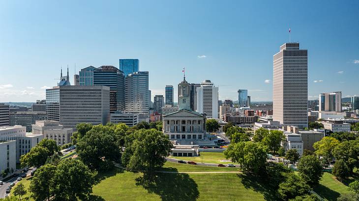 A green space with city buildings and a greek temple-style building behind it