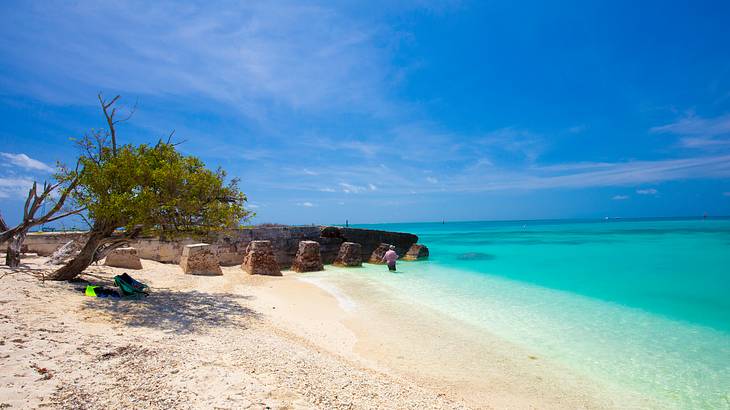 A white sand beach with trees and an old fort, the ocean, and a blue sky