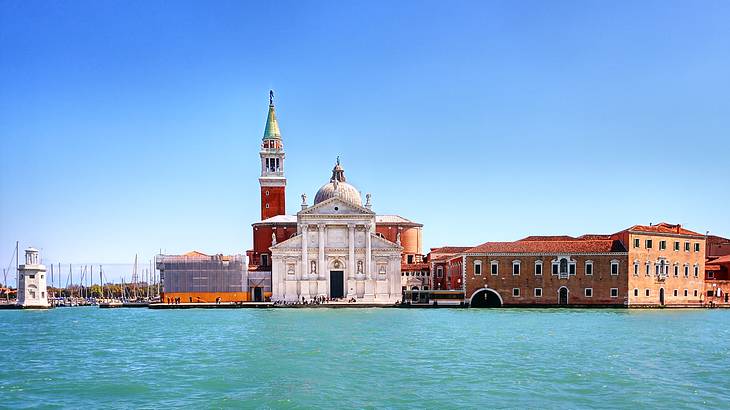 Looking across blue water at a tall tower and historic buildings with blue sky