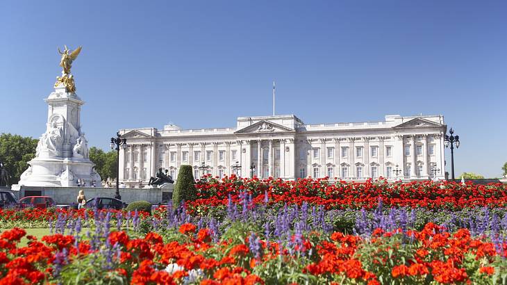 A white palace with a statue on the left, and red and purple flowers in front