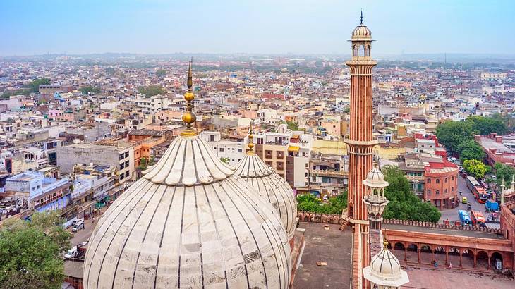 An aerial view of a city with two white domed mosques and a tower in the foreground