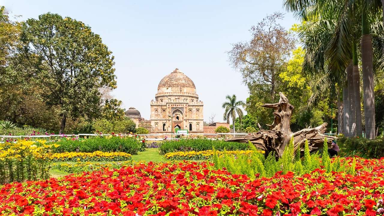 An ancient building with a domed roof in a garden with greenery and red flowers