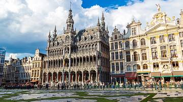 A Neo-Gothic and Baroque palace with grass, a street, and tourists in front of it