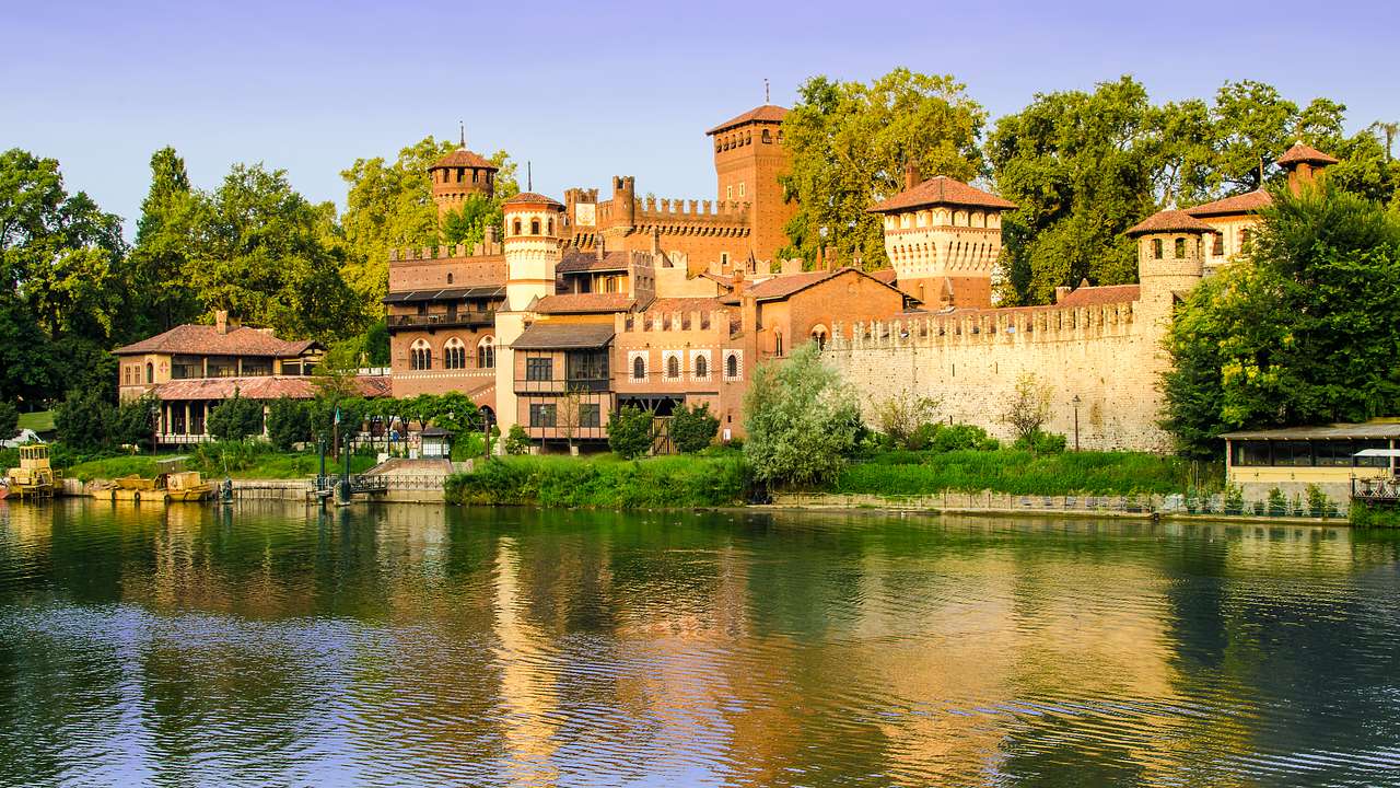A brown medieval castle surrounded by greenery overlooking the water