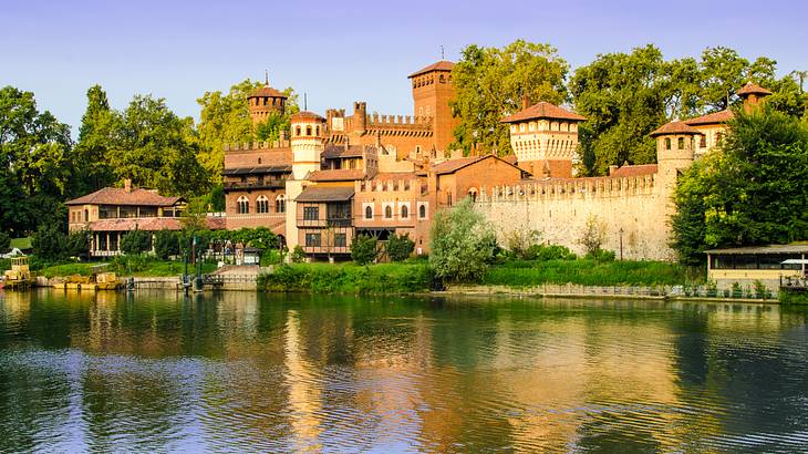 A brown medieval castle surrounded by greenery overlooking the water