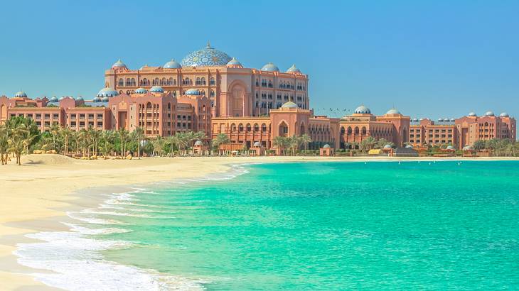 A brown palace with blue domes overlooking a beach with blue water