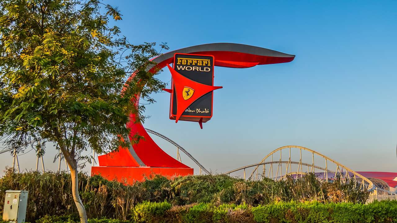A red sign that says "Ferrari World" with greenery and a tree below