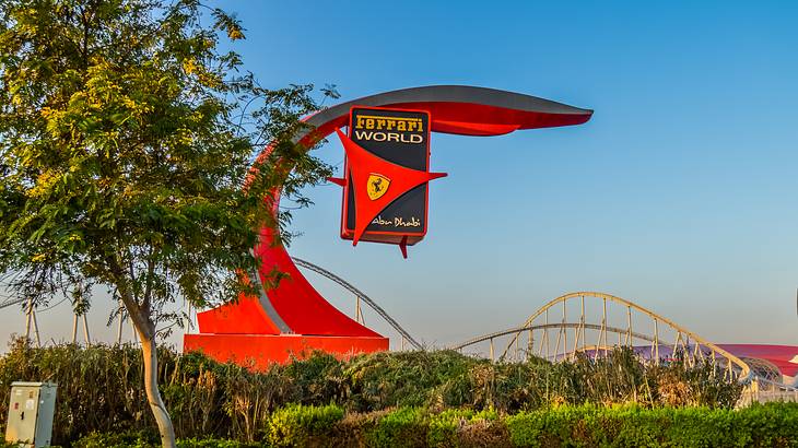 A red sign that says "Ferrari World" with greenery and a tree below