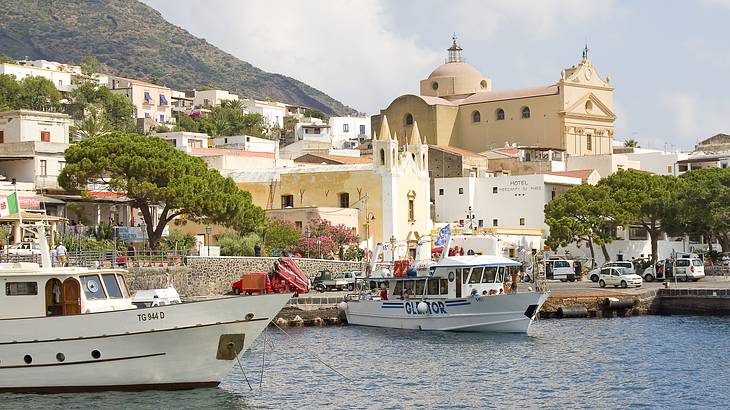 Two boats moored on a dock next to a town with old buildings and trees Two boats moored on a dock next to a town with old buildings and trees