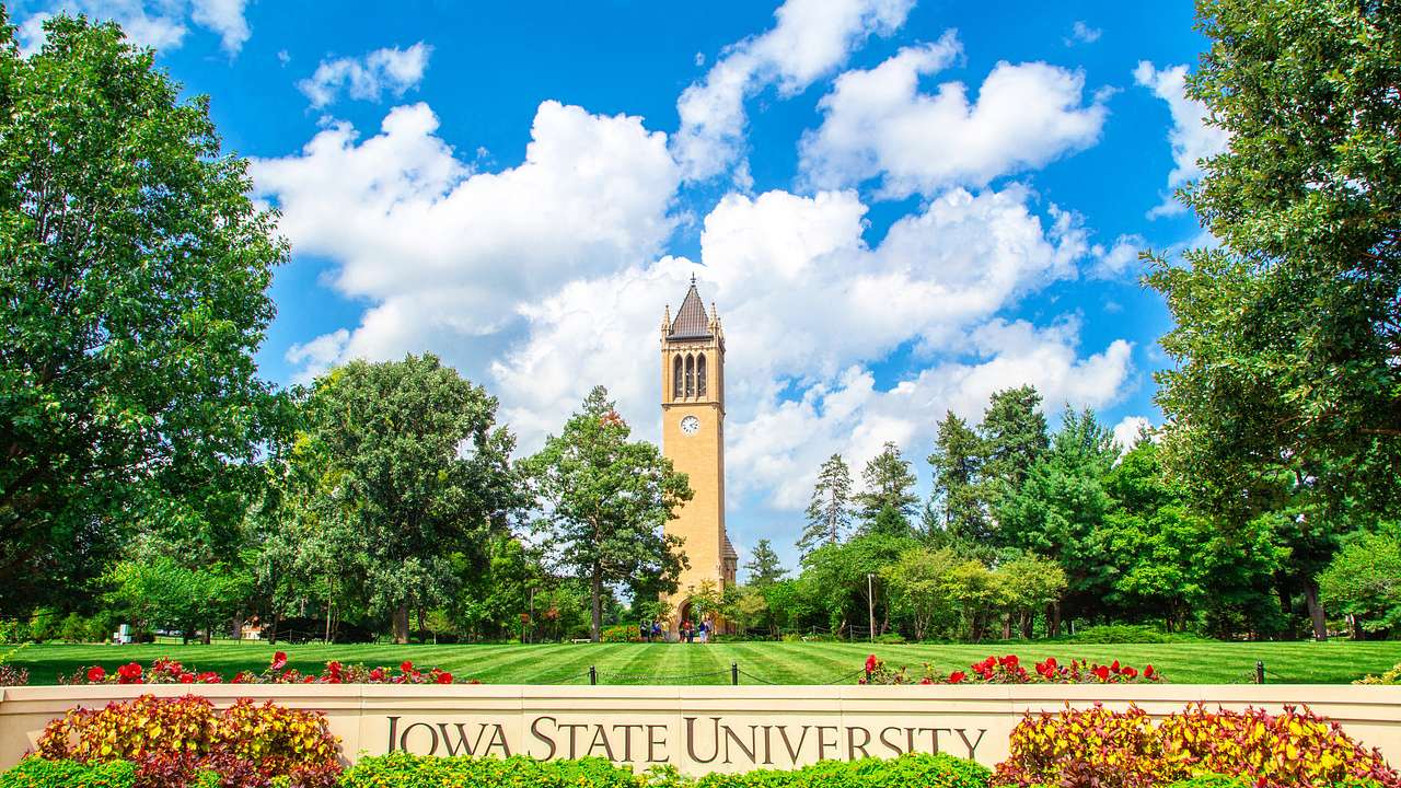 "Iowa State University" written on a wall against green grass and a clock tower