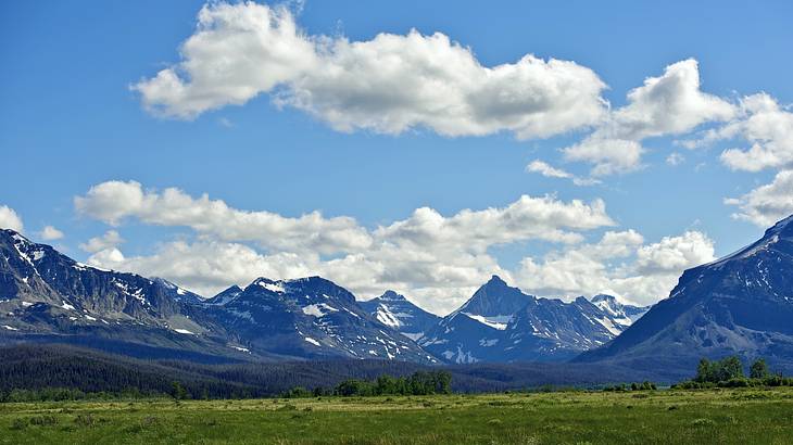 A green field at the base of rocky mountains with patches of snow A green field at the base of rocky mountains with patches of snow