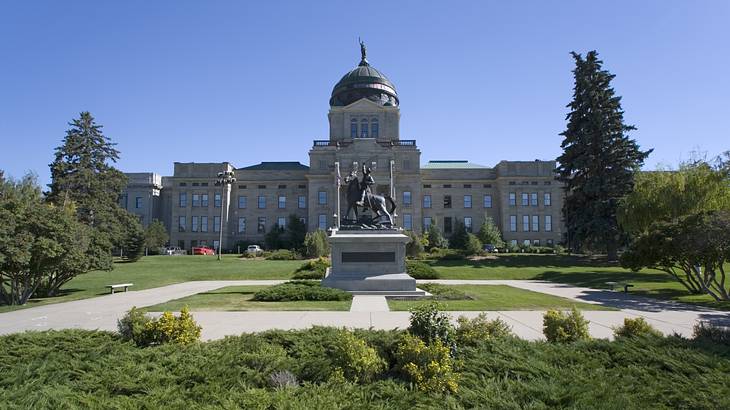 A bronze statue in front of a building with a copper dome surrounded by greenery
