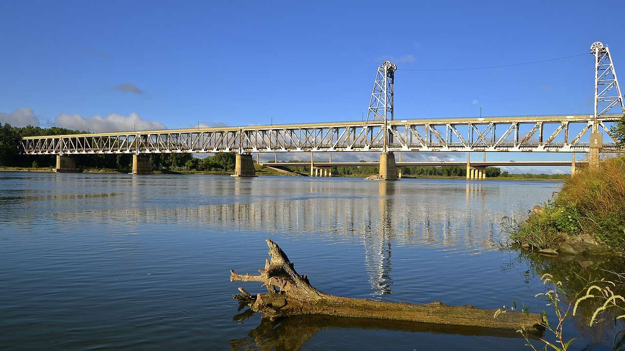 A cottonwood log on the shore of a river and a steel bridge in the back