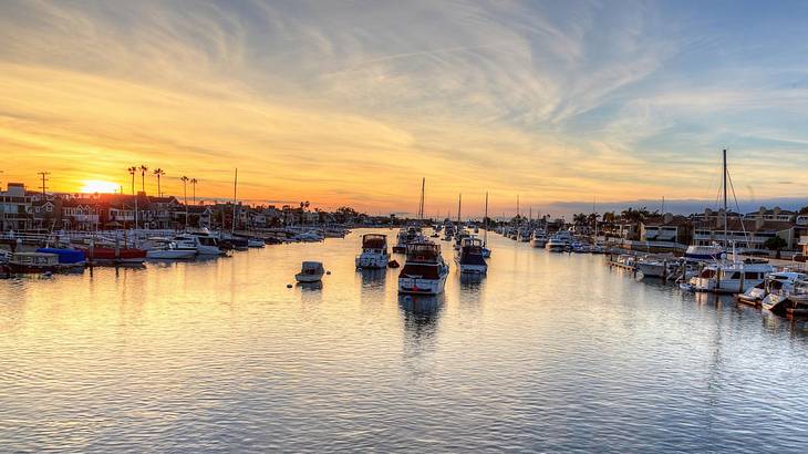 A waterway lined with docked boats and some boats idling on water in the middle