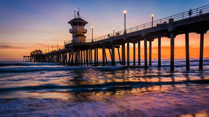 Sunset view over a pier above water, with lights and people walking on it