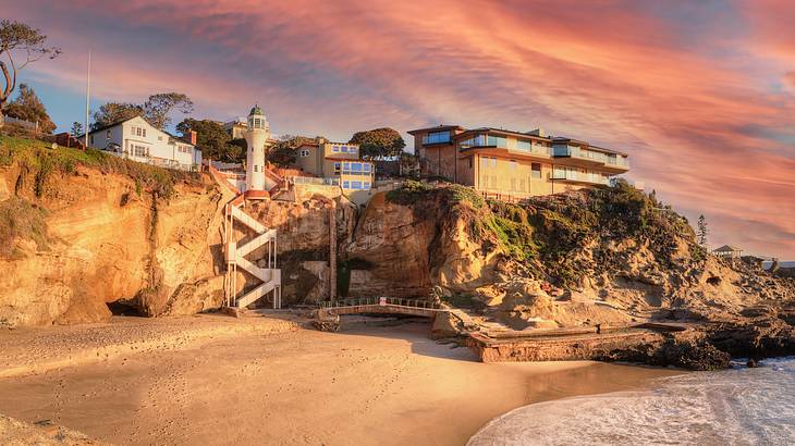 Cliff with houses overlooking the ocean and a sandy beach at sunset