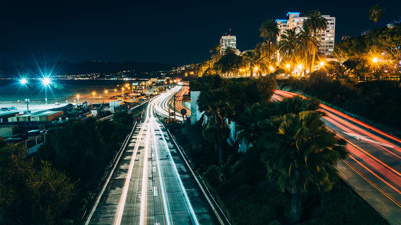 Aerial of a highway at night with lines of car lights, palms and buildings