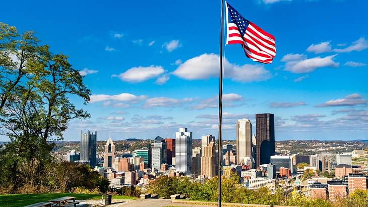 An American flag flying in a park with a skyline in front of it An American flag flying in a park with a skyline in front of it