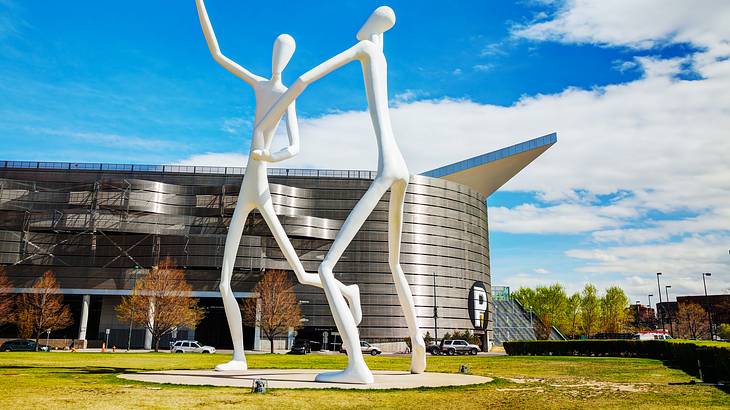 Two white statues on the grass in front of a metallic building Two white statues on the grass in front of a metallic building