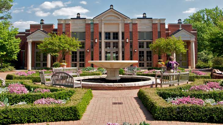 A redbrick and white building, a water fountain, and green and pink gardens