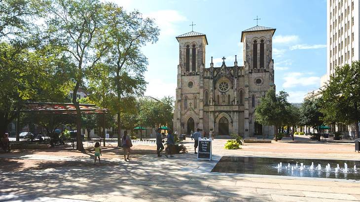 Looking across a plaza with trees at a gothic-style cathedral with crosses on top